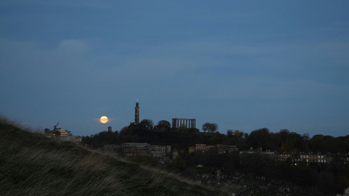 a full moon rises over a city skyline